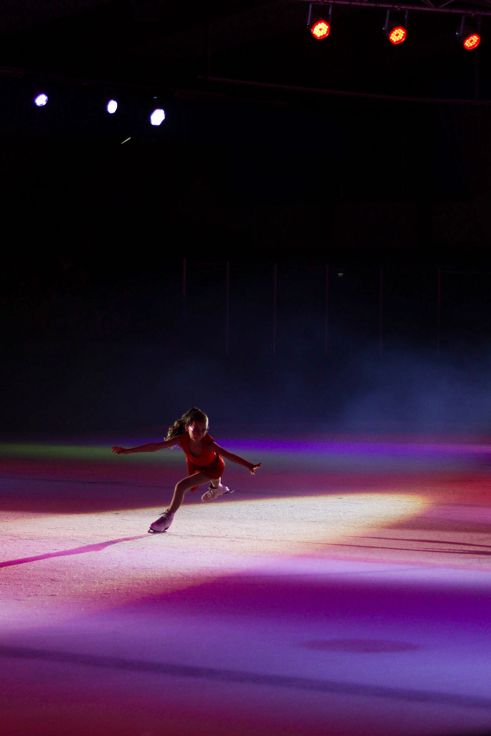 Petite patineuse à robe rouge sur la glace sous la lumière des projecteurs très colorés