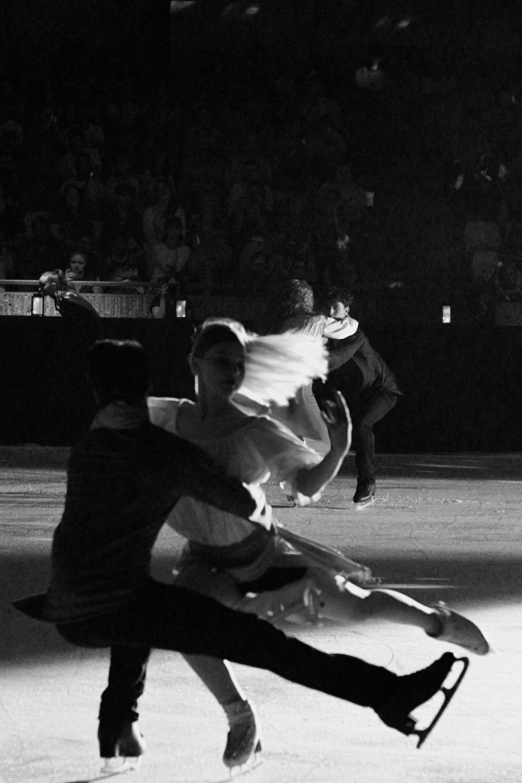 Photographie noir et blanc de deux couples de patineurs sur la glace, s'enlacent, un couple en premier plan, et le deuxième au dernier blanc