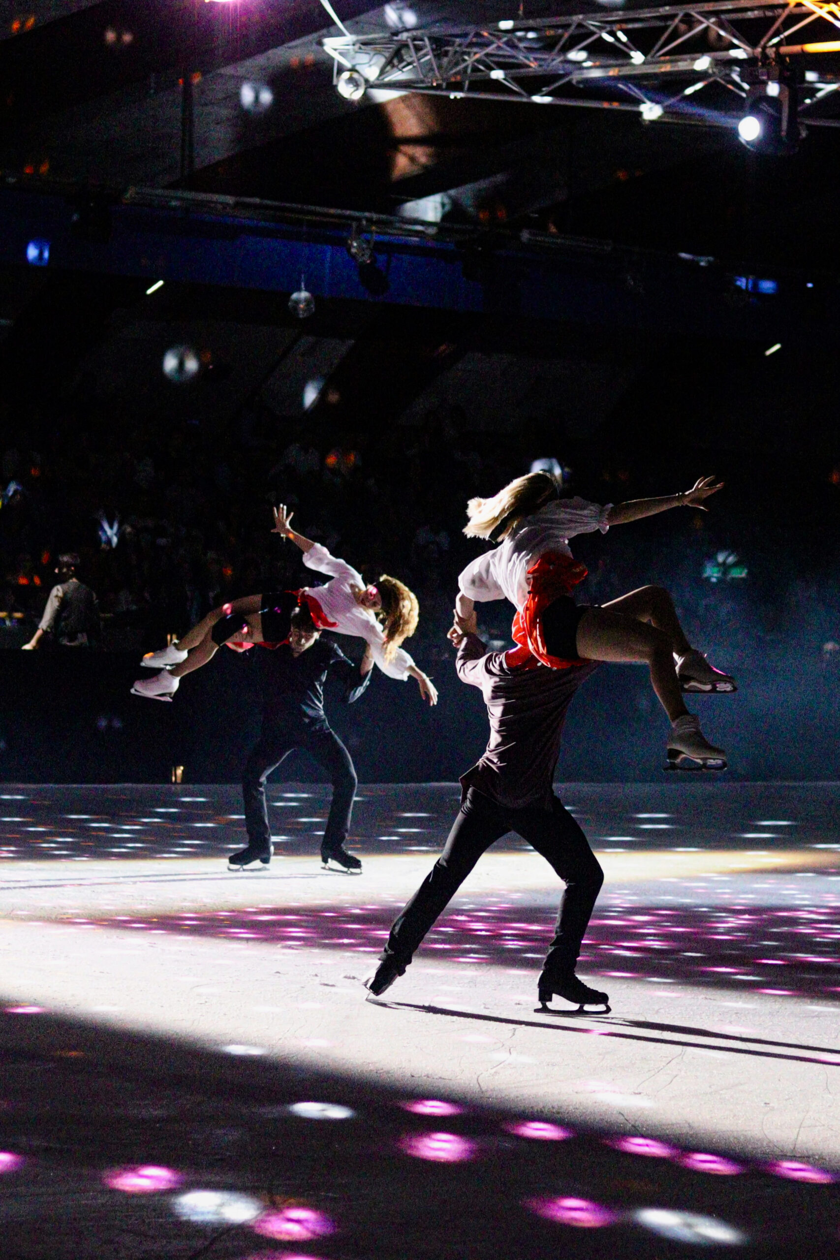 Photographie noir et blanc de deux couples de patineurs sur la glace, réalisant une figure avec les patineuses en l'air, un couple en premier plan, et le deuxième au dernier blanc