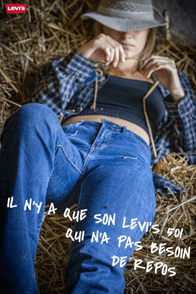 Femme style cow boy allongé sur une bonne de paille avec un chapeau sur ses yeux pendant une sieste. Avec comme slogan "Il n'y a que son Levi's 501 qui n'a pas besoin de repos"